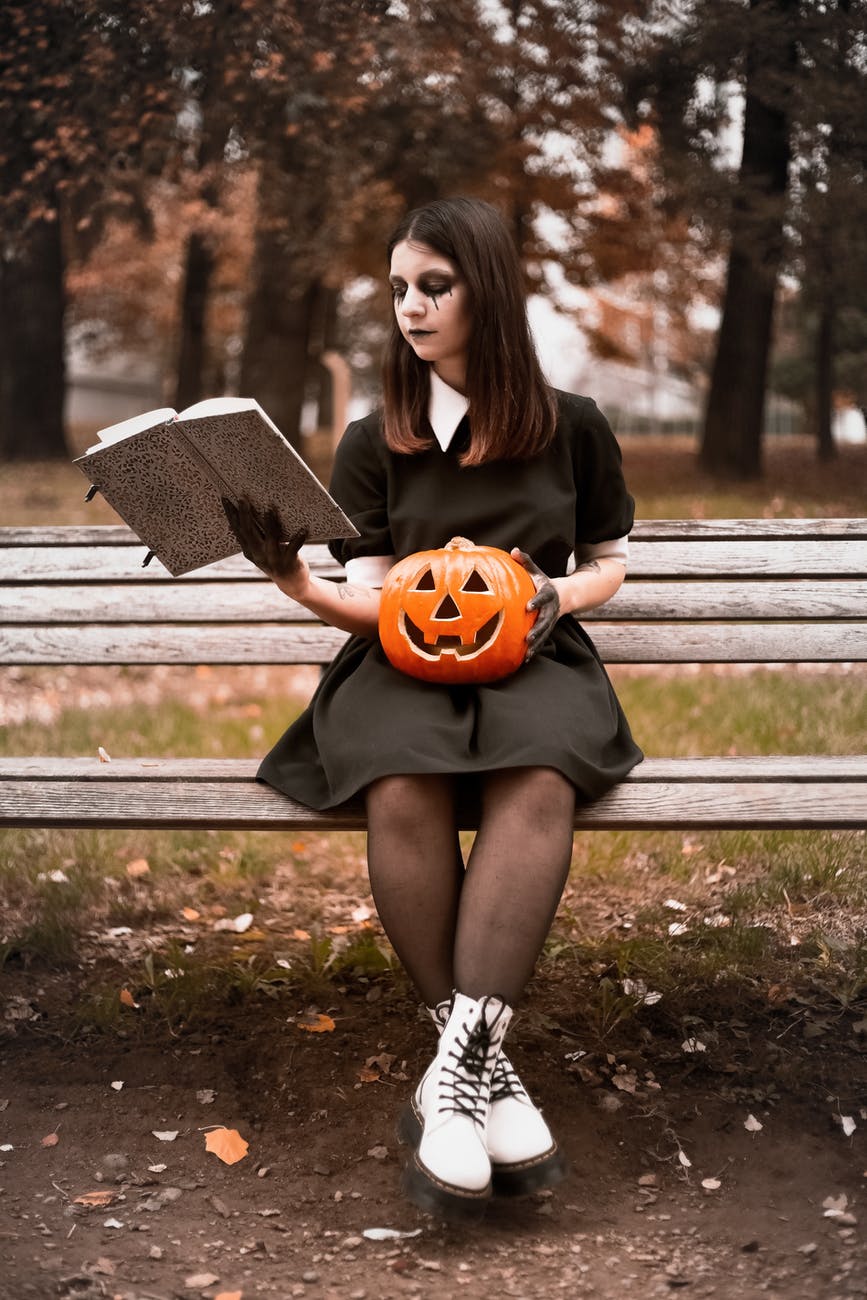 woman in black long sleeve shirt sitting on bench holding jack o lantern